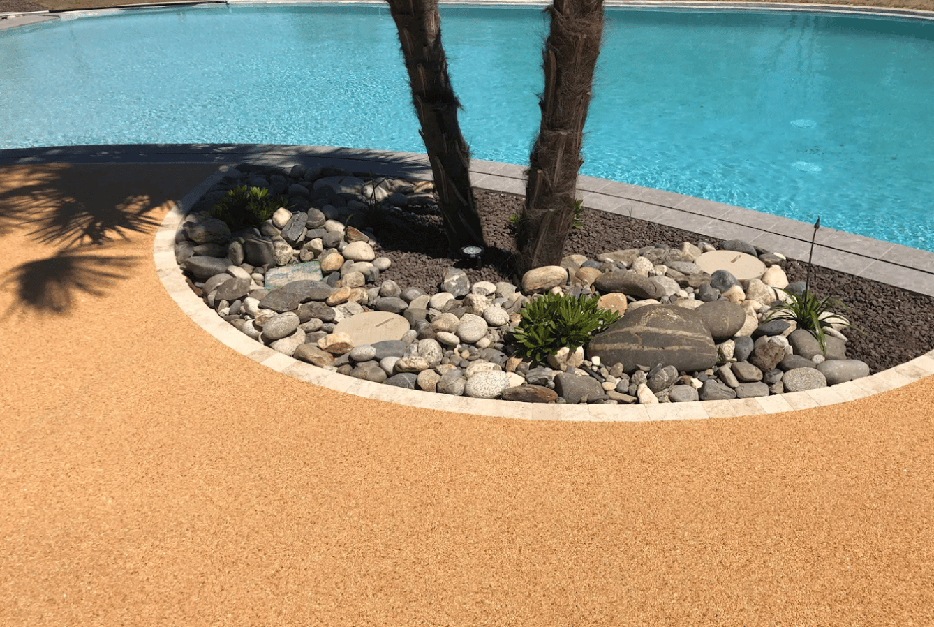 Plage de piscine en moquette de pierre ocre avec galets et plantations