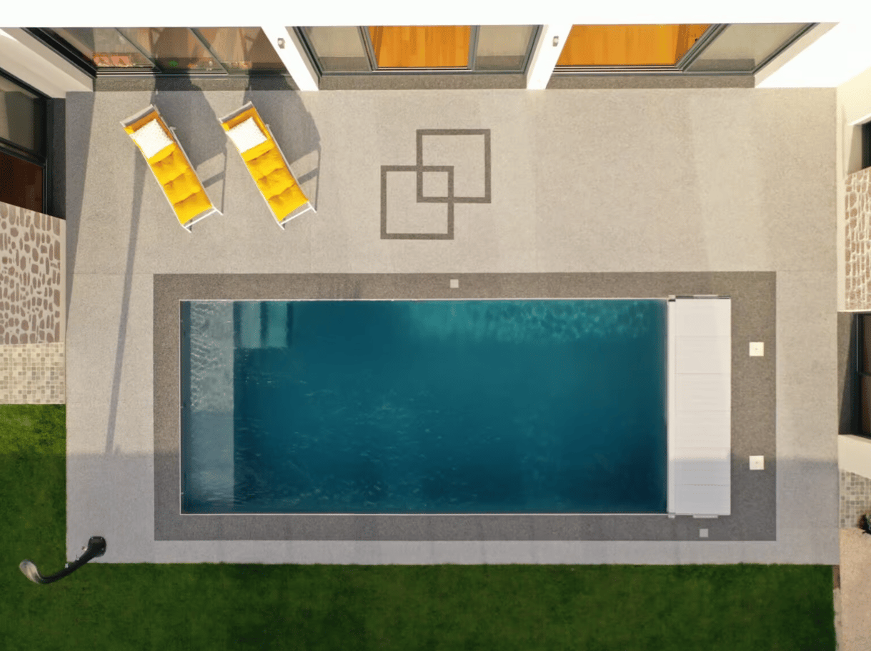 Terrasse grise en moquette de pierre autour d’une piscine, vue de dessus