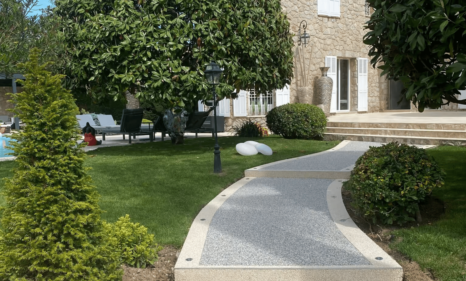 Allée courbe en moquette de pierre grise devant une maison et un jardin